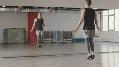 Athlete man jumping on skipping rope at cardio training in gym club