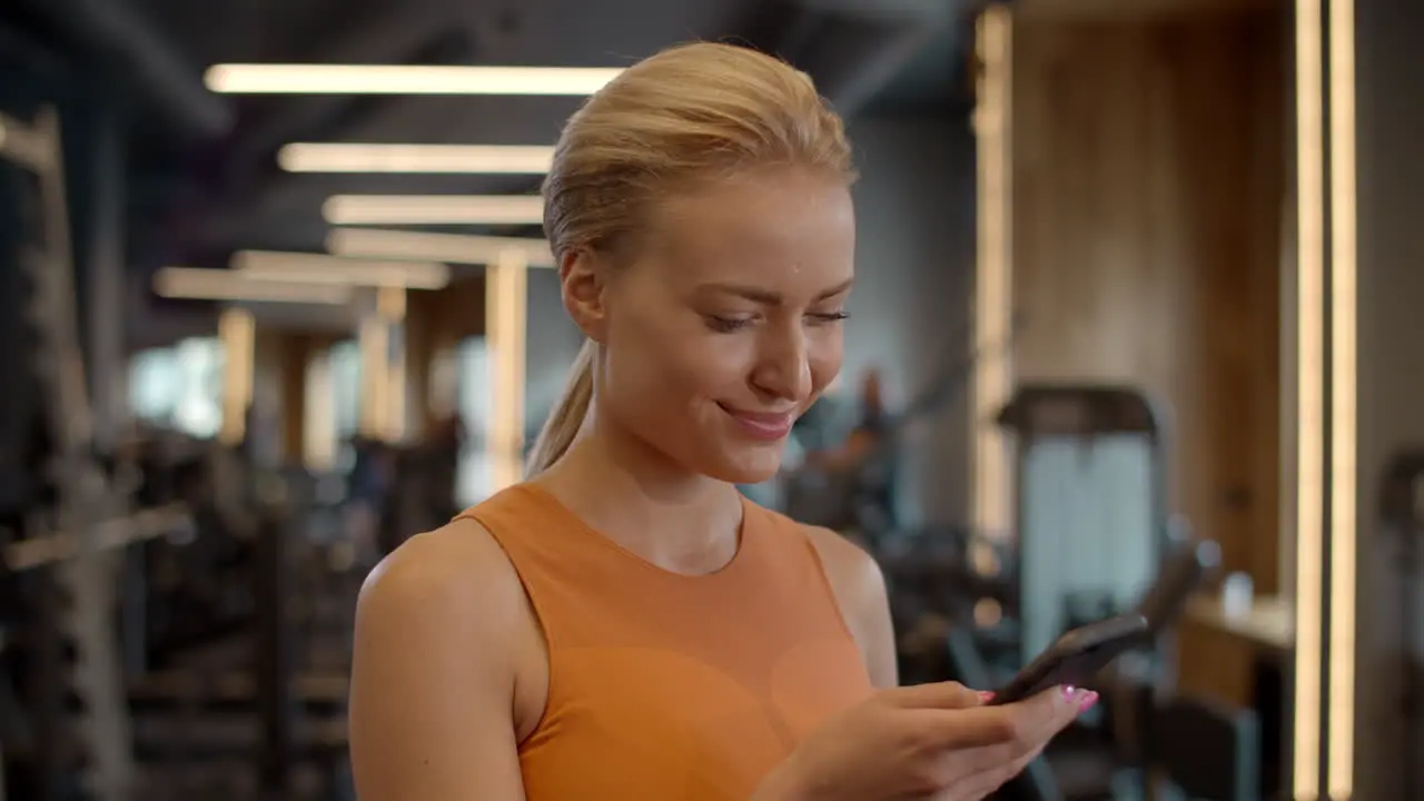 Romantic sportswoman texting message in sport club Athlete girl standing at gym