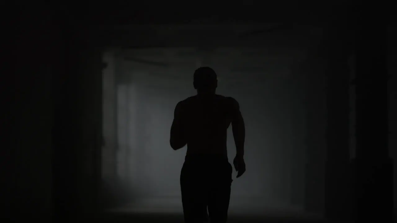 Fitness man running in dark corridor Male jogger training in loft building