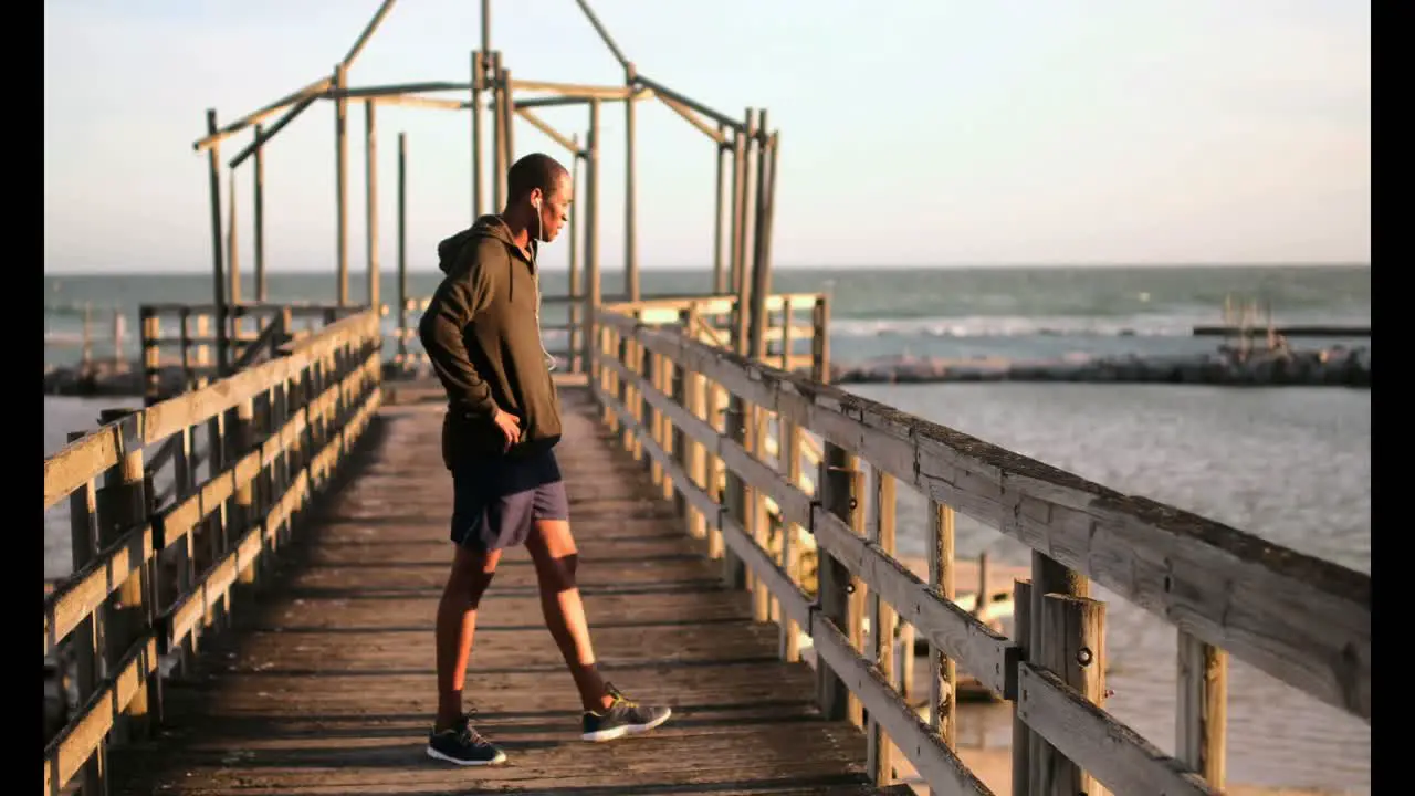 African American male jogger walking on pier at beach in the sunshine 4k