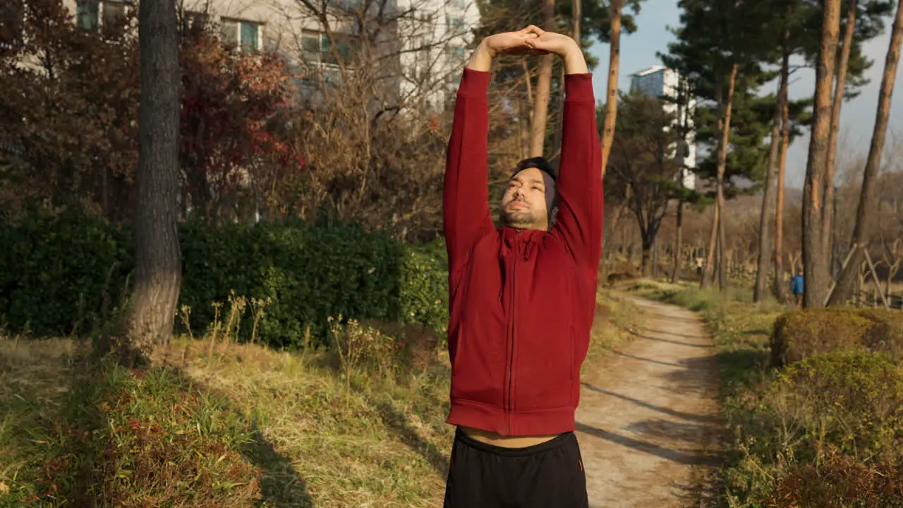 Mid Adult Man Active Exercising Outdoors in a Park Trail Stretching Torso Locking Arm Above Head and Jumping with Warming up Shoulders Rotations Outdoors at Apartment Park in Autumn slow motion