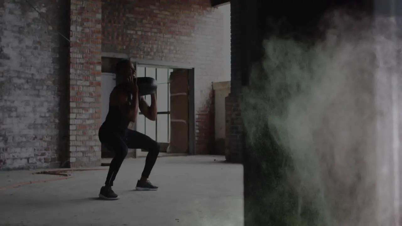 Colorful dust explosion against african american man performing squat exercise using medicine ball