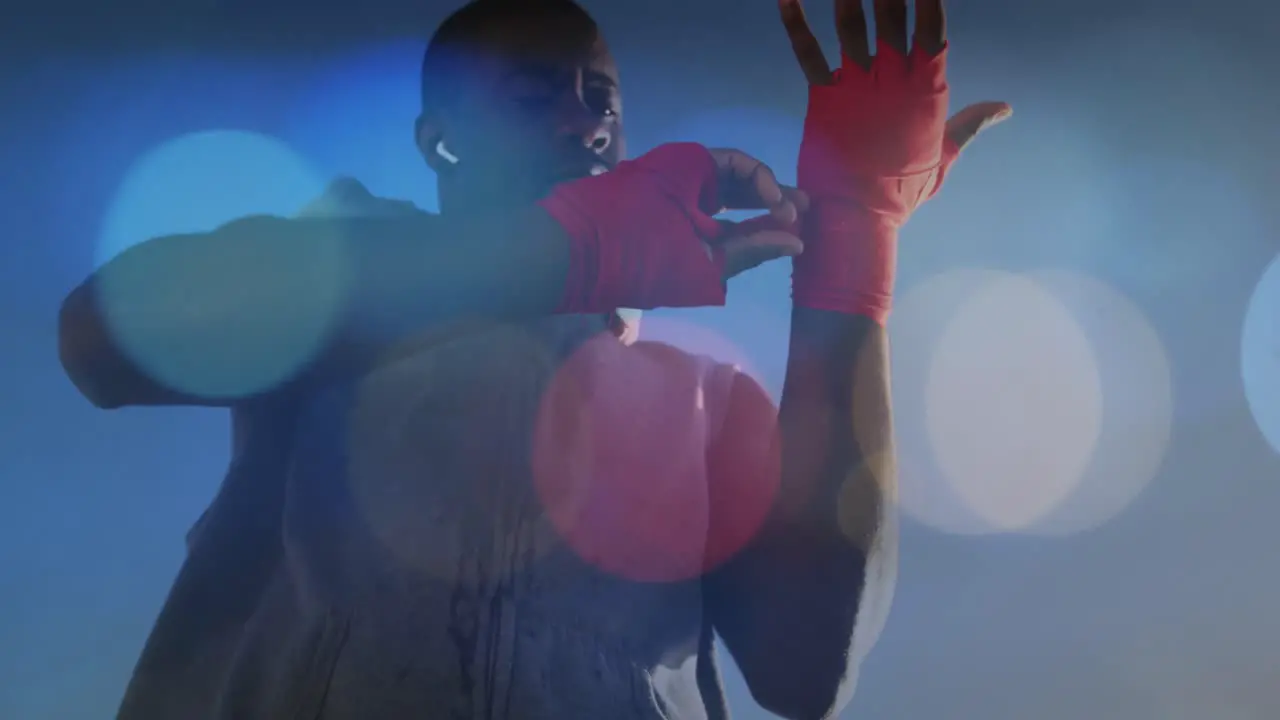 Colorful spots of light against african american male boxer applying bondage tape on hands