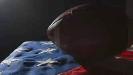 Low Key Lighting Studio Shot Of American Football On Stars And Stripes Flag 