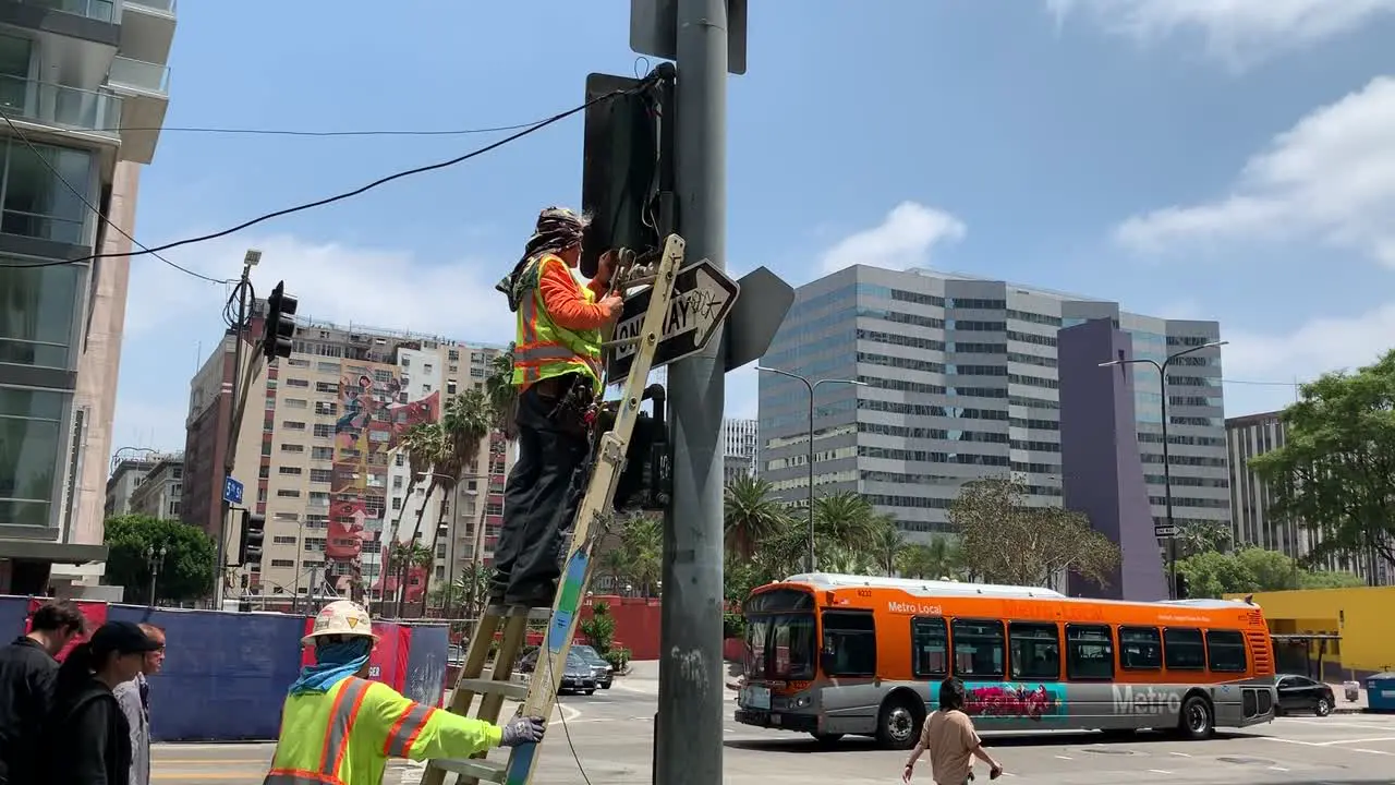 A professional repair man on a portable ladder using tools to fix a broken traffic signal light on the busy intersection of Pershing Square in downtown Los Angeles