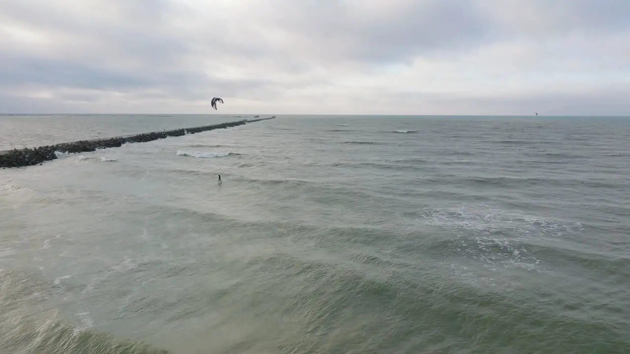 Establishing aerial view of a man engaged in kitesurfing overcast winter day high waves extreme sport Baltic Sea Karosta beach  wide drone shot moving forward