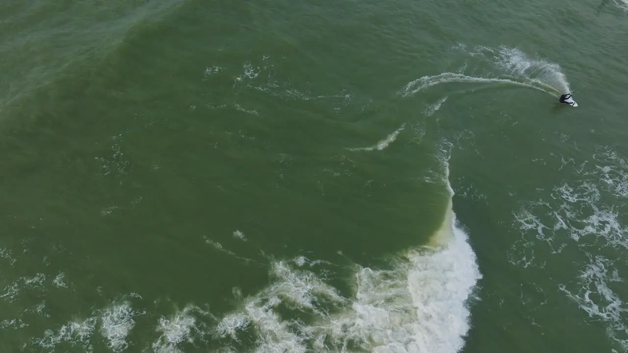 Establishing aerial birdseye view of a man engaged in kitesurfing overcast winter day high waves extreme sport Baltic Sea Karosta beach  drone dolly shot moving right