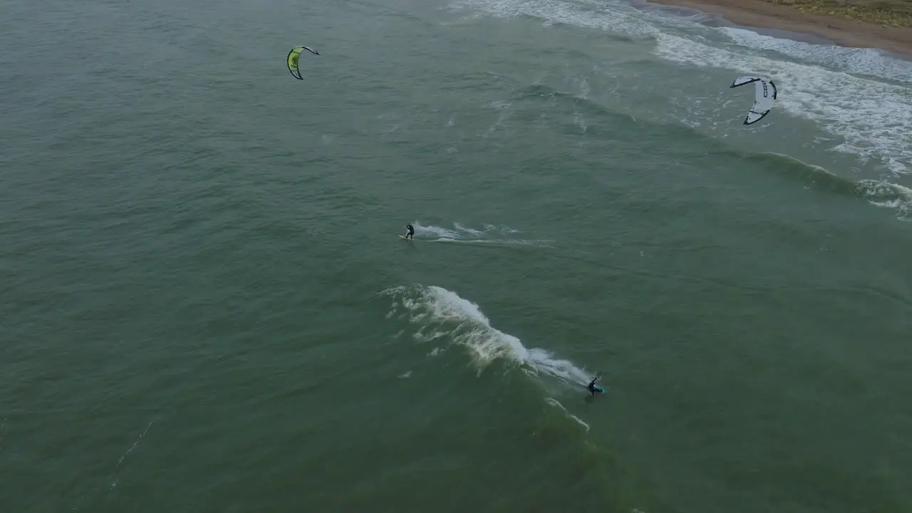 Establishing aerial view of a group of people engaged in kitesurfing overcast winter day high waves extreme sport Baltic Sea Karosta beach  drone birdseye shot moving forward tilt down