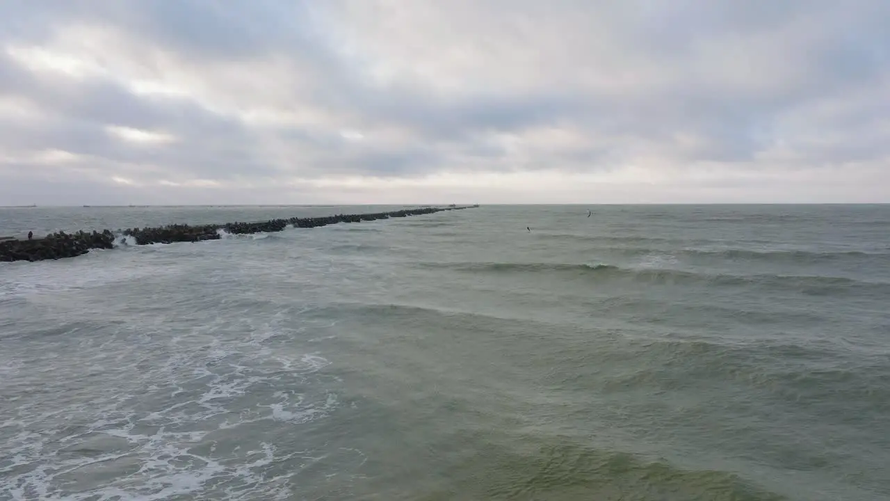 Establishing aerial view of a man engaged in kitesurfing overcast winter day high waves extreme sport Baltic Sea Karosta beach  stone pier on the left drone shot moving forward