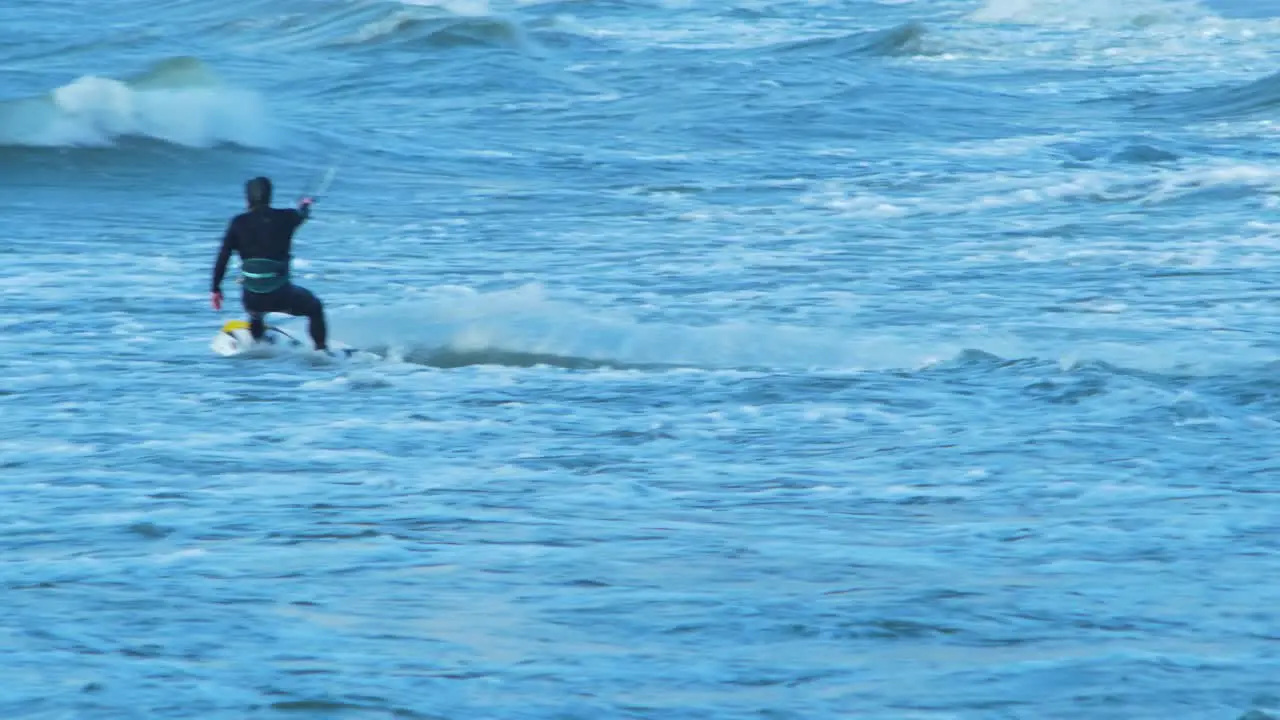 Man engaged in kitesurfing in sunny autumn day high waves jump over the wave Baltic Sea Karosta beach in Liepaja medium shot