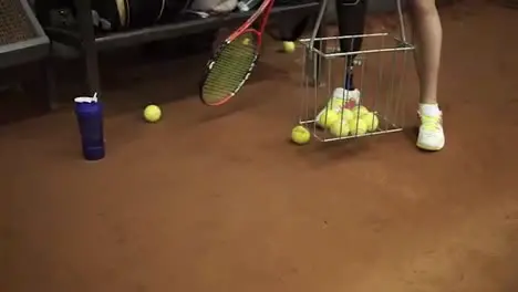 Athlete disabled female collects tennis balls in the basket helping herself with a racket Close up