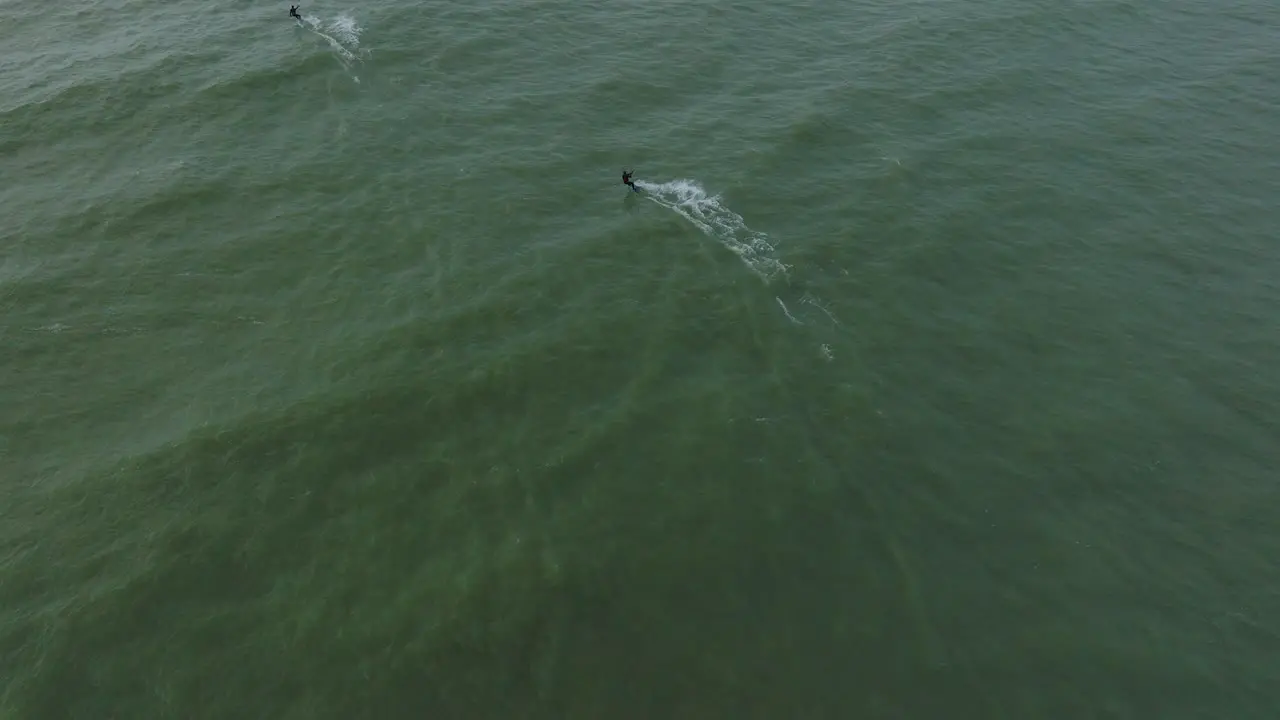 Establishing aerial view of a group of people engaged in kitesurfing overcast winter day high waves extreme sport Baltic Sea Karosta beach  birdseye drone shot moving forward