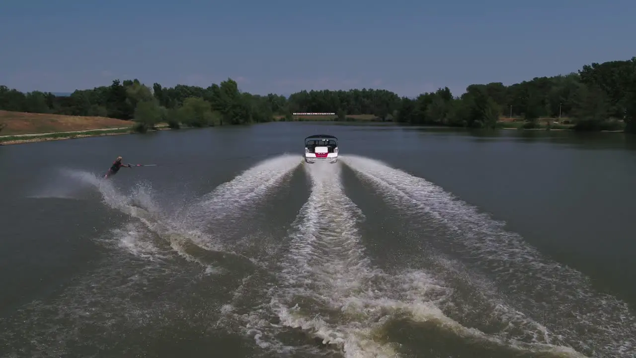 Person slaloms with water ski pulled by a speedboat tracking shot