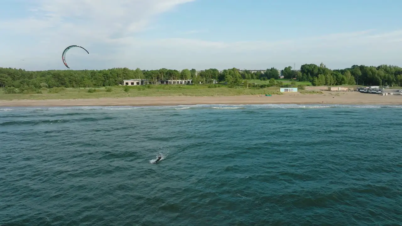 Establishing aerial view of a group of people engaged in kitesurfing sunny summer day high waves extreme sport Baltic Sea Karosta beach  wide drone shot moving backward