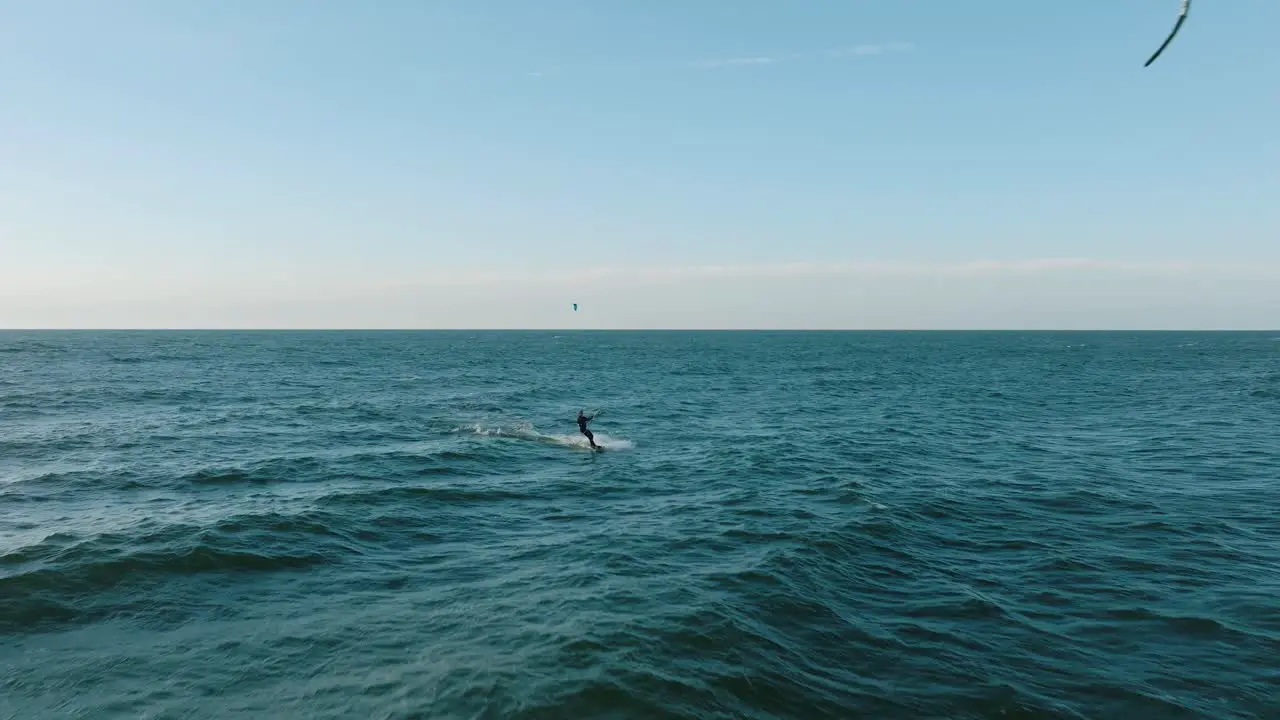 Establishing aerial view of a group of people engaged in kitesurfing sunny summer day high waves extreme sport Baltic Sea Karosta beach  wide drone shot moving forward low