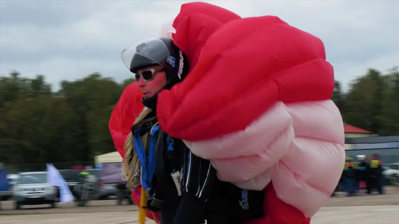 Professional caucasian male skydiver taking his red parachute after a successful landing overcast summer day medium handheld tracking shot