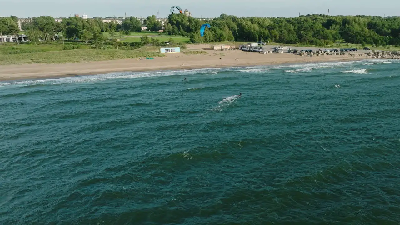 Establishing aerial view of a group of people engaged in kitesurfing sunny summer day high waves extreme sport Baltic Sea Karosta beach  wide drone shot moving forward