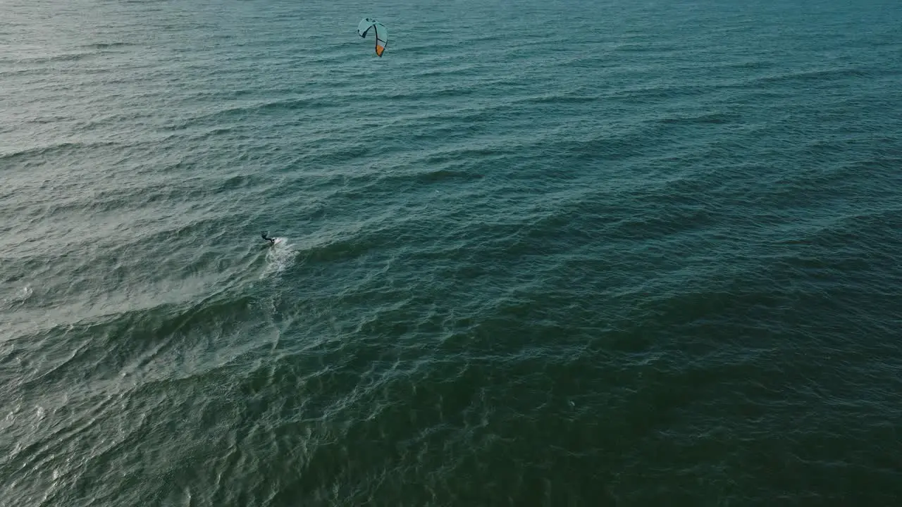 Establishing aerial view of a group of people engaged in kitesurfing sunny summer day high waves extreme sport Baltic Sea Karosta beach  wide birdseye drone shot moving forward