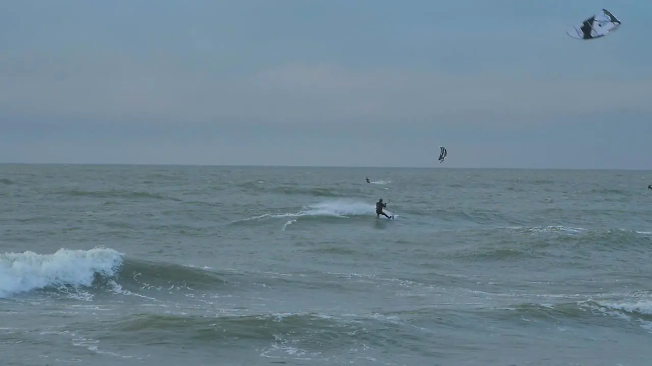 A group of people engaged in kitesurfing overcast winter day high waves Baltic Sea Karosta beach  slow motion wide shot