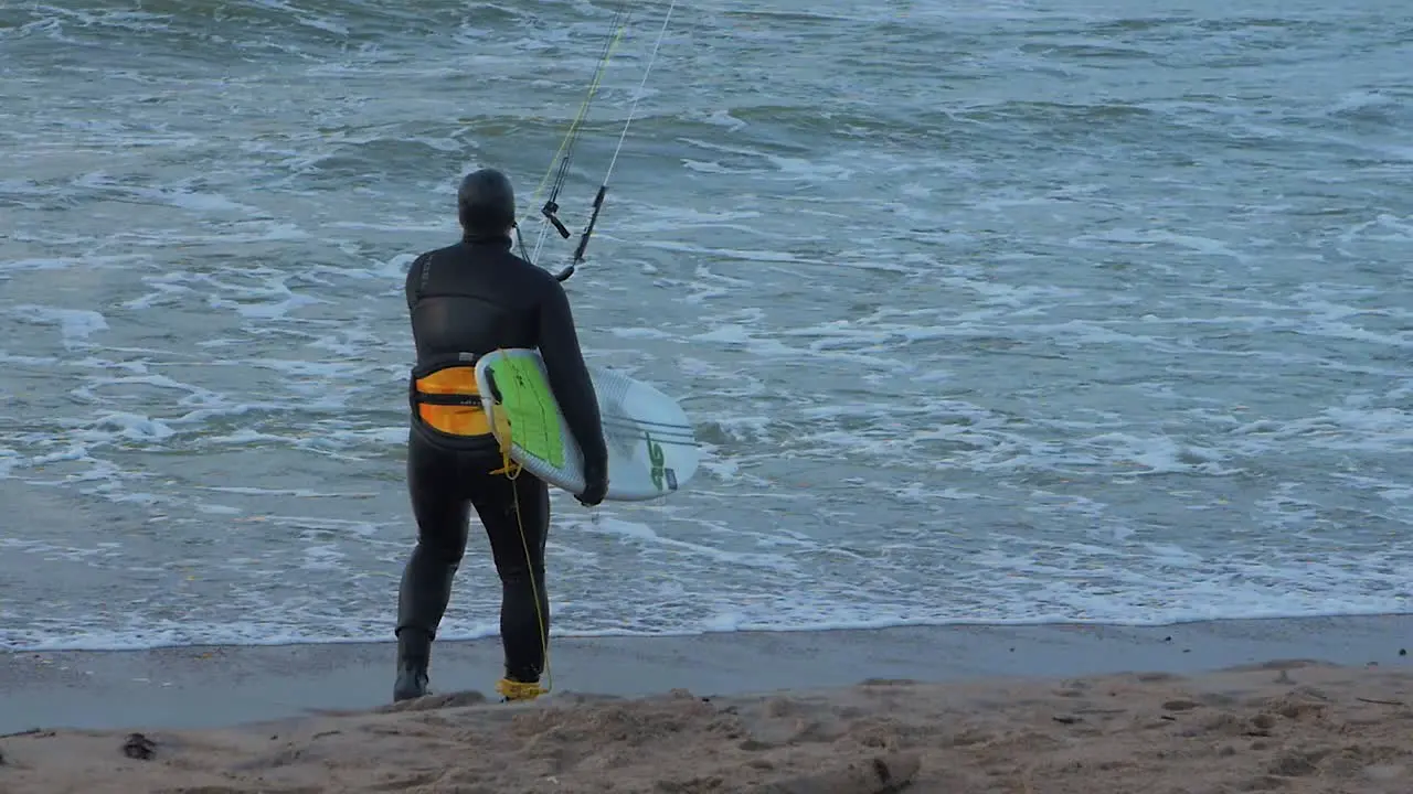 Man engaged in kitesurfing overcast winter day high waves Baltic Sea Karosta beach  slow motion medium shot