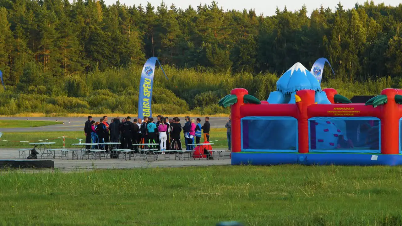 Group of professional skydivers in jumpsuits discussing after a successful high altitude parachute jump sunny summer evening golden hour medium distant shot