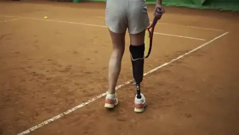 Attractive tall disabled woman plays tennis makes a ball pitch Long haired in grey shorts and sports bra Indoors