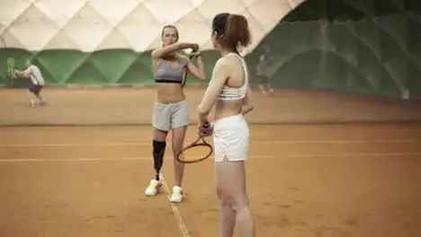 A beautiful athletic invalid girl teaches the beginner of the correct trajectory of a racket hit in tennis Other players on the background Slow motion