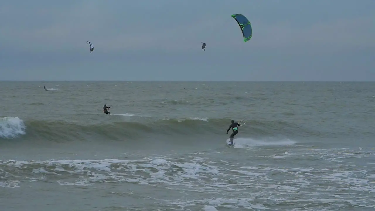 A group of people engaged in kitesurfing overcast winter day high waves Baltic Sea Karosta beach  slow motion distant shot