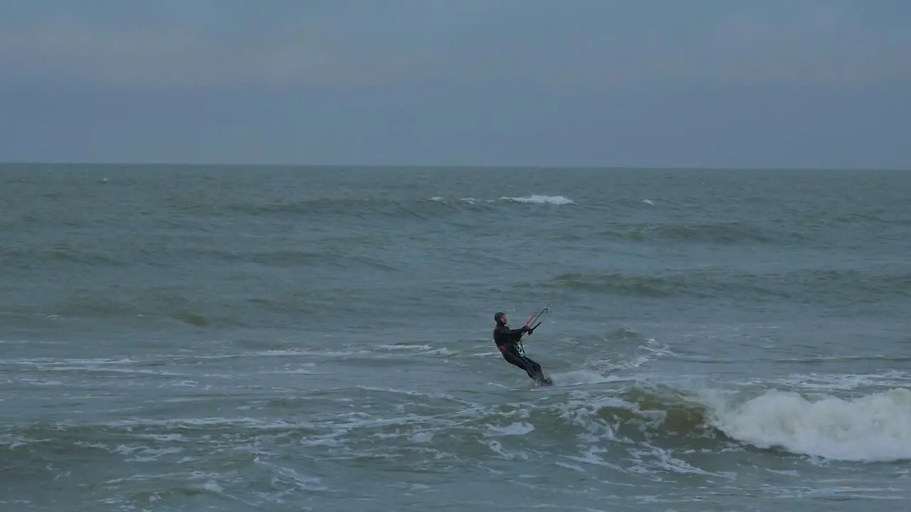 Active man engaged in kitesurfing overcast winter day high waves Baltic Sea Karosta beach  slow motion distant medium shot