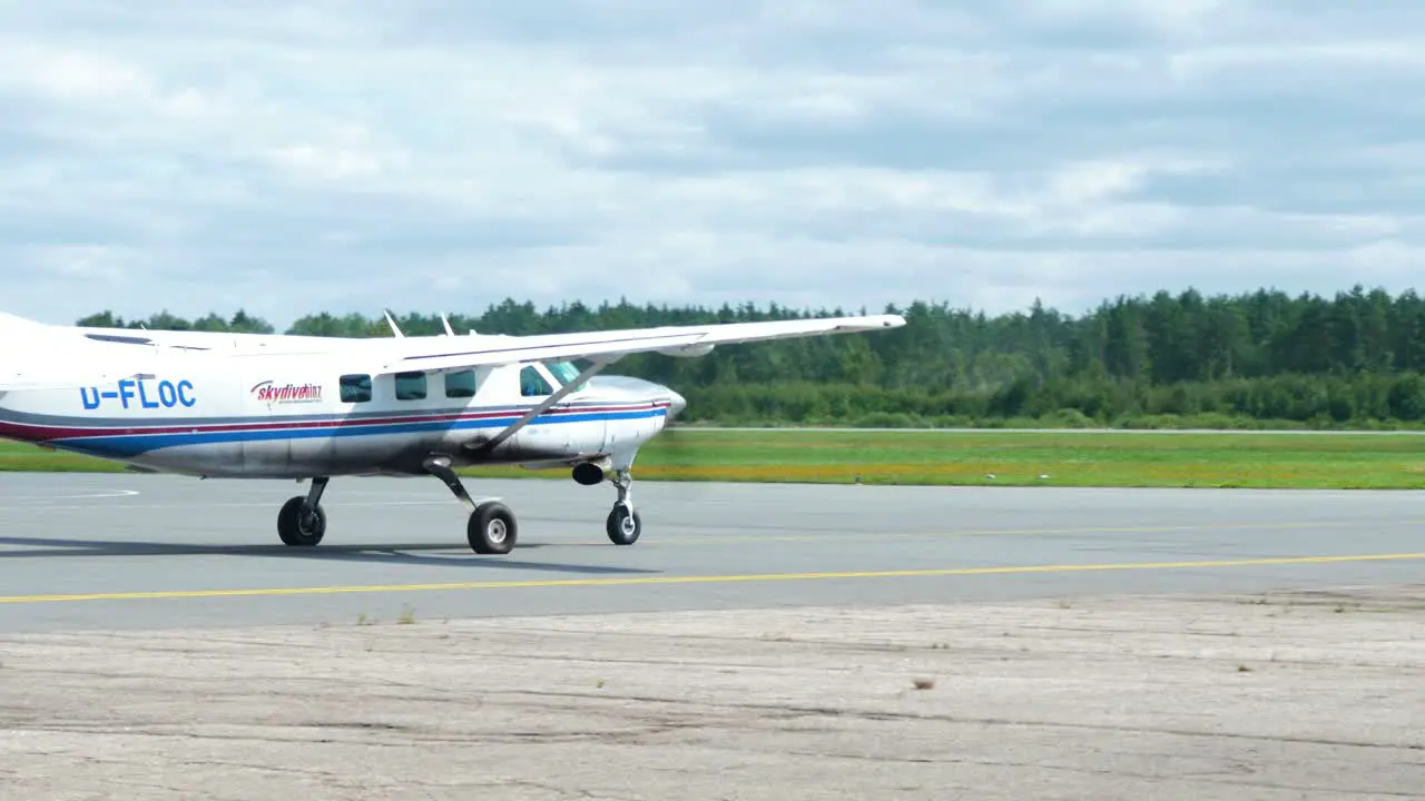 White skydiver plane taxiing on an airport runway before taking off taking professional skydivers up in the sky for a parachute jump summer day distant medium tracking shot