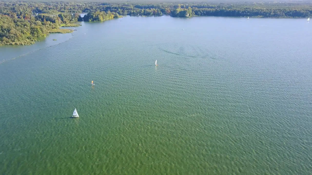 drone flying above a lake with sailing boats and windsurfers casting big shadows