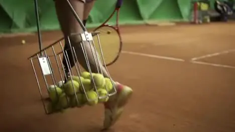 Aiming footage of a disabled woman's legs Slender girl collects balls with a tennis basket Indoors tennis court