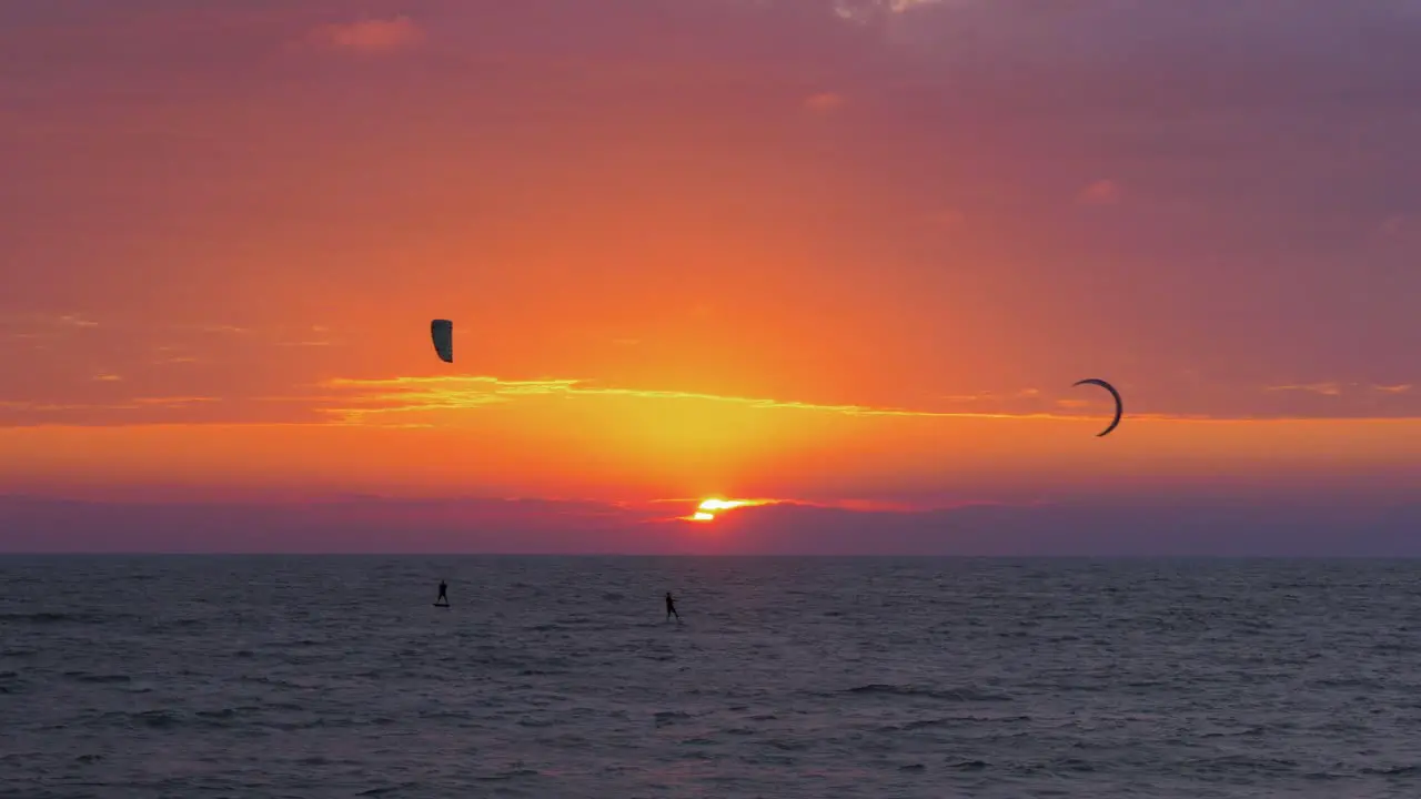 Silhouette of people engaged in kitesurfing in vibrant summer evening just before sun goes down high contrast beautiful red sunset Baltic Sea coastline Karosta beach in Liepaja wide distant shot