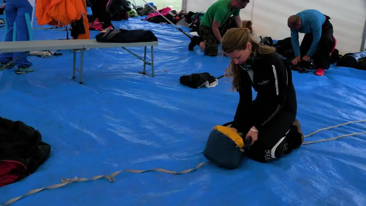 Professional caucasian brunette female skydiver in black jumsuit packing her parachute on the ground medium handheld shot