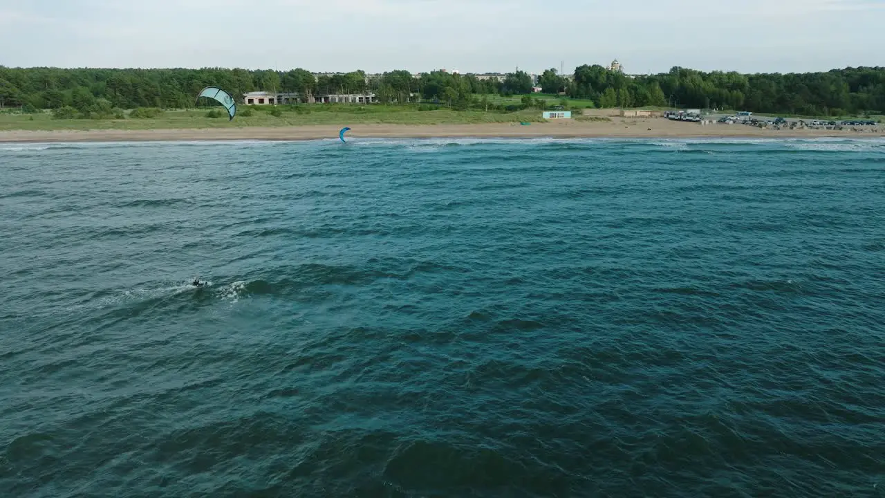 Establishing aerial view of a group of people engaged in kitesurfing sunny summer day high waves extreme sport Baltic Sea Karosta beach  wide drone shot moving forward tilt down