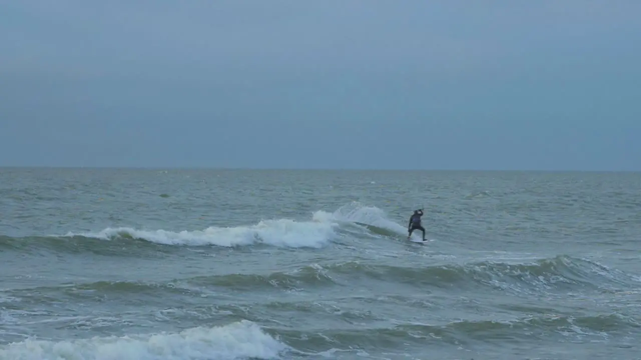 Man engaged in kitesurfing overcast winter day high waves Baltic Sea Karosta beach  slow motion distant medium shot