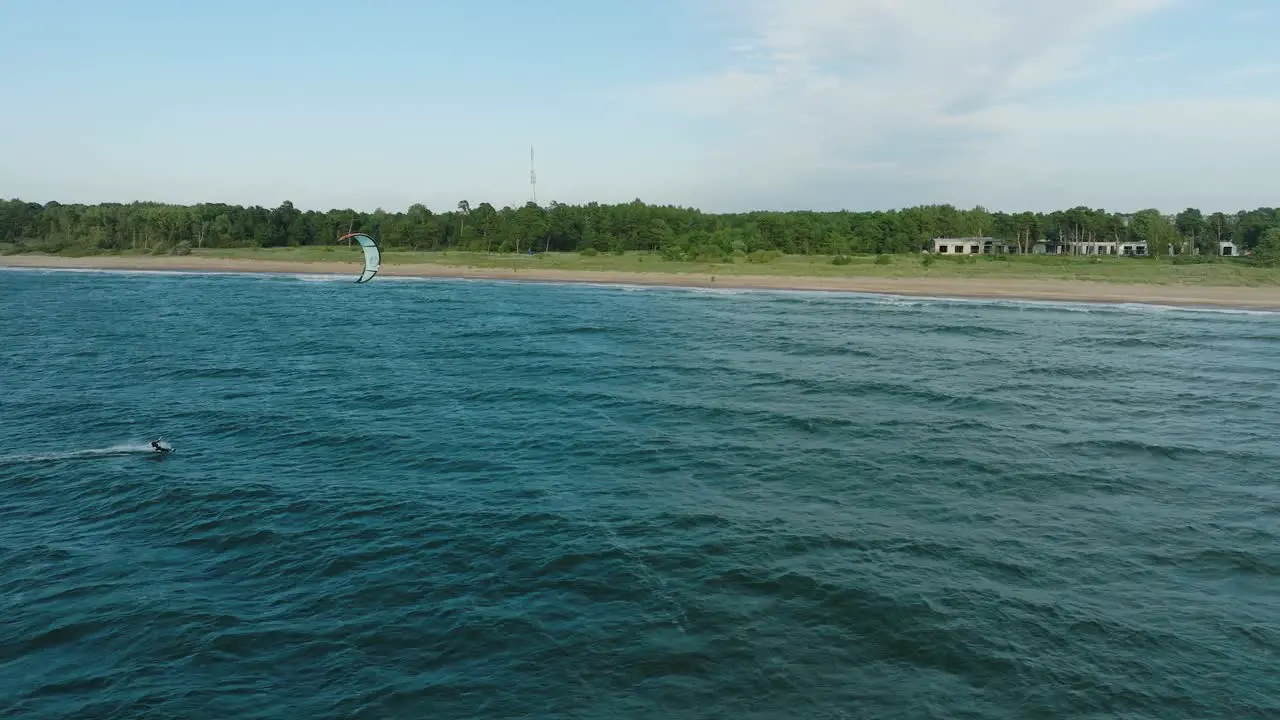 Establishing aerial view of a group of people engaged in kitesurfing sunny summer day high waves extreme sport Baltic Sea Karosta beach  wide drone dolly shot moving right