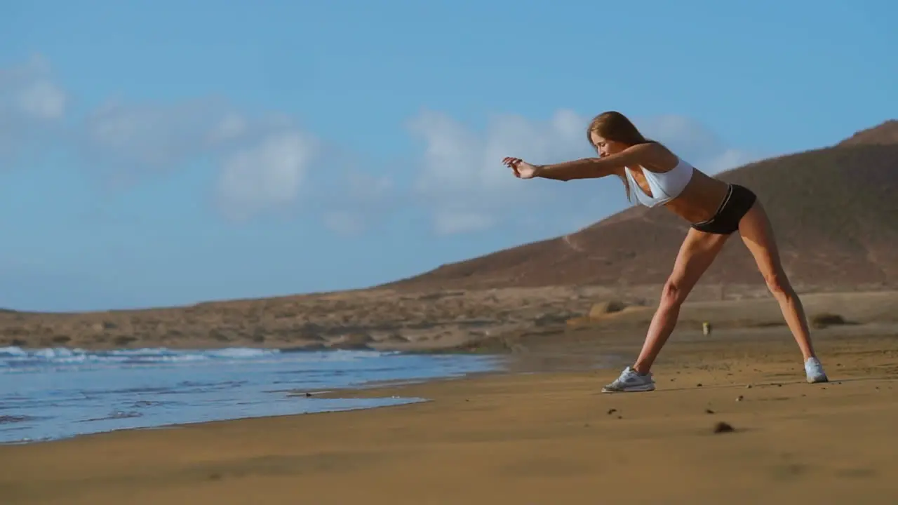 Woman stretching legs and hamstrings doing Standing Forward Bend Yoga stretch pose on beach Fitness woman relaxing and practising sport and yoga on