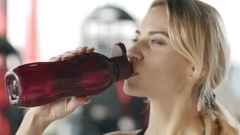 Smiling sport woman drinking water in fitness gym Happy girl sipping water