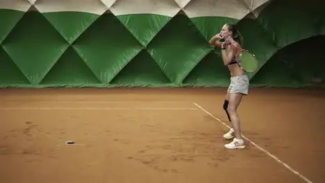 Backside view of energetic young woman with a prosthesis down her knee is focused on beating the ball on an elastic band Indoors