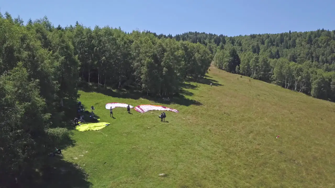 Group of adventurers stands on the launch site preparing for flight while paragliding