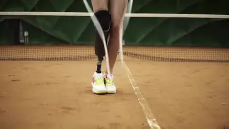 Close up footage of a slender girl with a right leg prosthesis jumping rope on a tennis court in sneakers Indoors