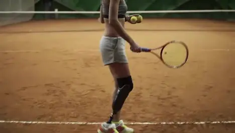 Back side footage of a pretty young woman with leg prosthesis playing tennis with the rival Ball serving Slow motion