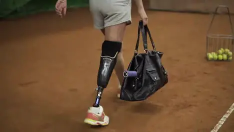 Attractive injured girl with a sports bag in her hands comes to the indoor tennis court to train Making first ball serve Slow motion