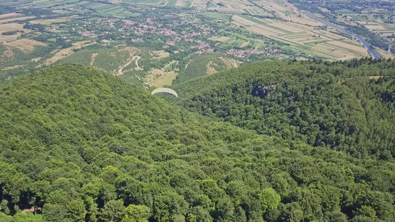 Scenic view of paragliding over green trees with valley and town at base of mountain