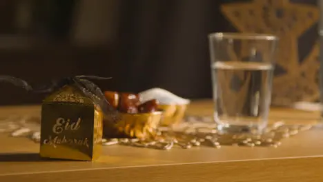 Bowl Of Dates With Glass Of Water And Gift Boxes On Table In Muslim Home Celebrating Eid 2