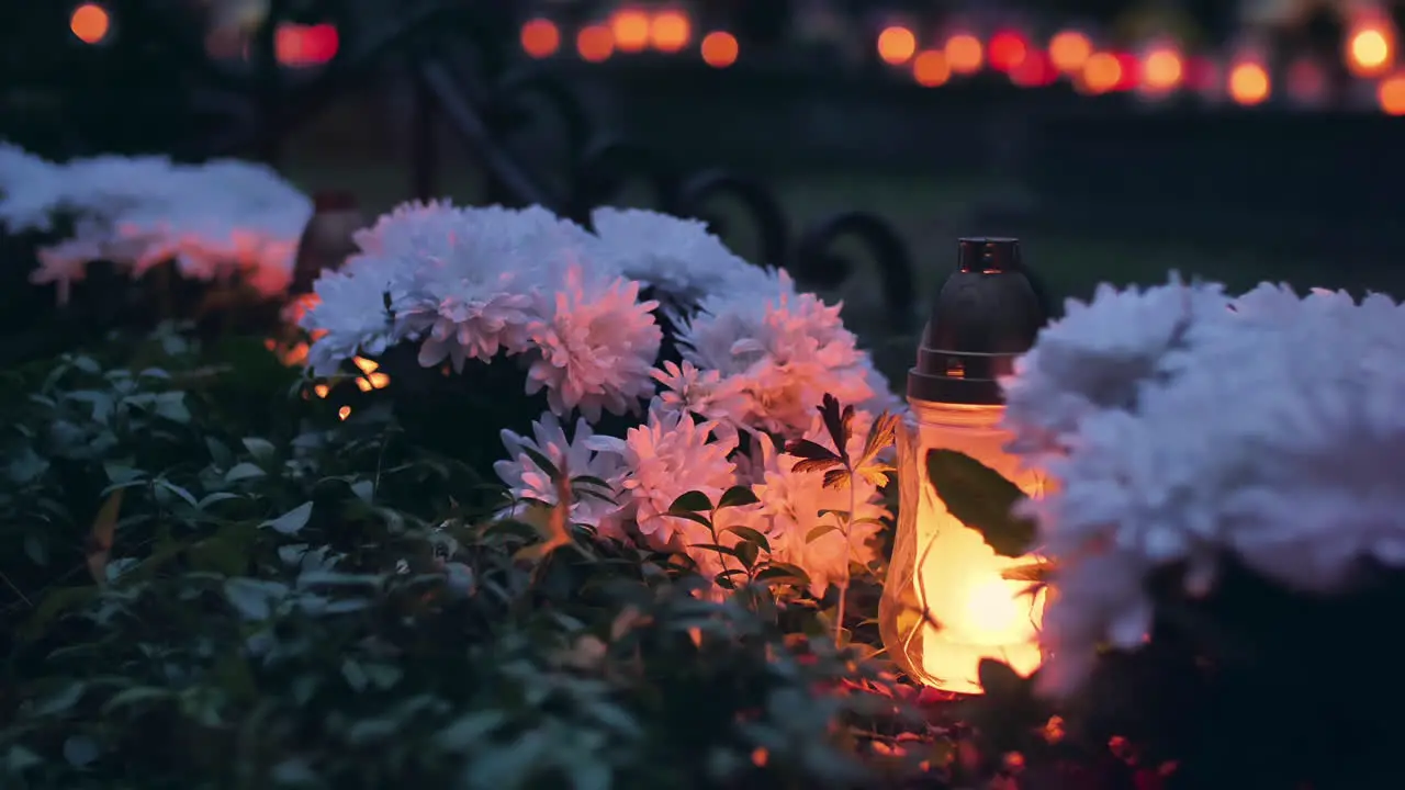 Grave with white flowers lit by burning grave candle