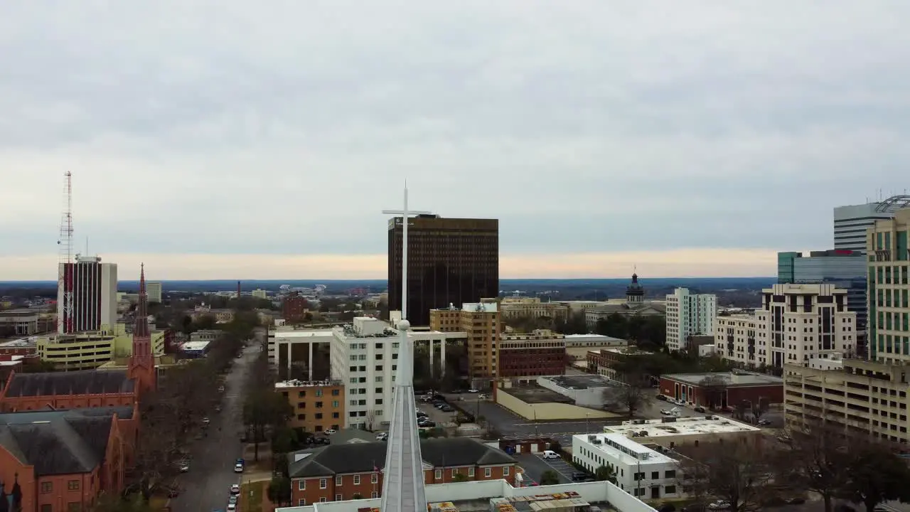 A drone shot of a white cross on a steeple with the Comubia state capital building in the background