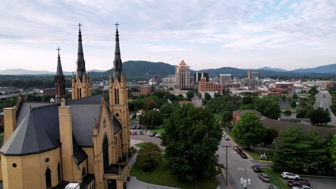 aerial push over roman catholic church with roanoke virginia skyline in background