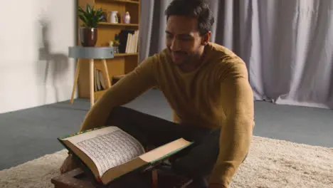 Muslim Man At Home Sitting On Floor And Reciting From The Quran